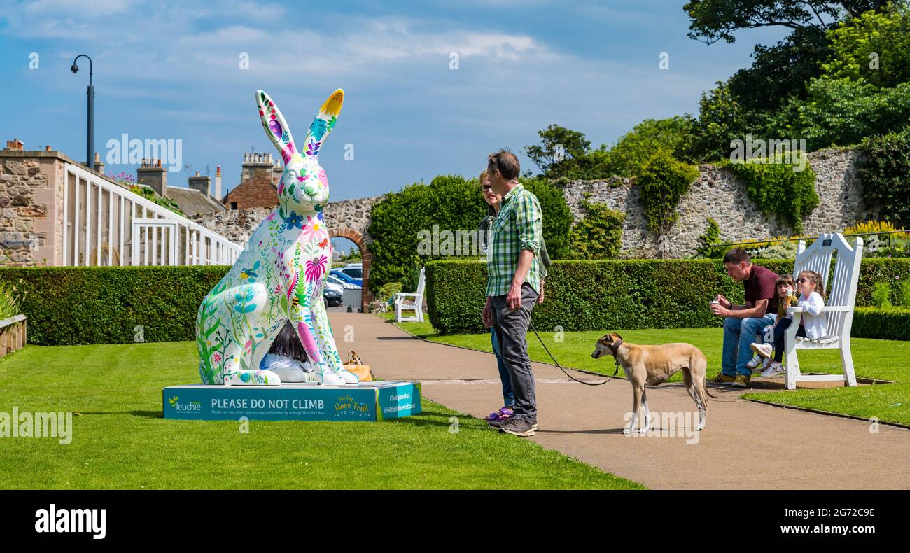 North Berwick, East Lothian, Scozia, Regno Unito, 10 luglio 2021. Il Big Hare Trail: Il sentiero inizia oggi e durerà 11 settimane con 10 gigantesche sculture di lepre dipinte a mano, ciascuna di un artista diverso, situate intorno alla città balneare. È organizzato da Leuchie House, una tregua di carità per le persone con disturbi neurologici. Nella foto: La gente ammira una lepre dipinta da Rosie Watson nel parco Lodge Grounds Foto Stock