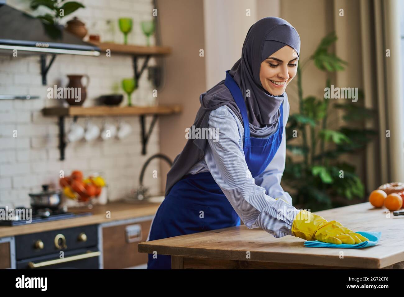 Gioiosa donna musulmana che pulisce un tavolo in cucina Foto Stock