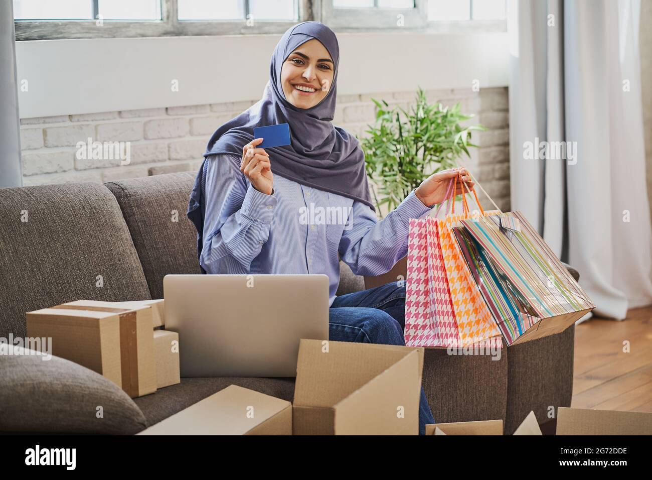 Donna musulmana felice che tiene una carta e un mazzo di borse regalo Foto Stock