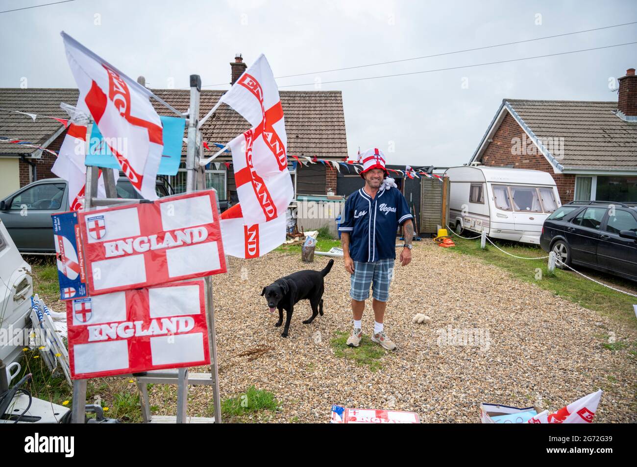 Trimingham, North Norfolk, Regno Unito. 10 luglio 2021. Un uomo vende bandiere, cappelli, cartelli e altri souvenir del suo vialetto d'ingresso in Inghilterra, prima della finale dei Campionati europei di calcio dell'Inghilterra V Italia a Wembley. Credit: Julian Eales/Alamy Live News Foto Stock