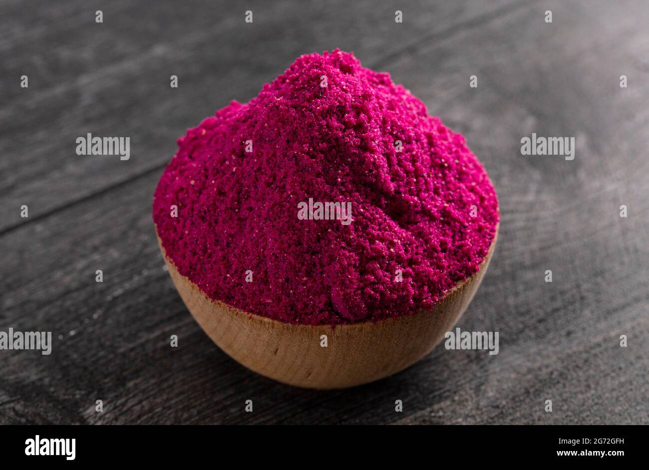 Polvere di Dragonfruit rosa brillante su un bancone di legno nero Foto Stock