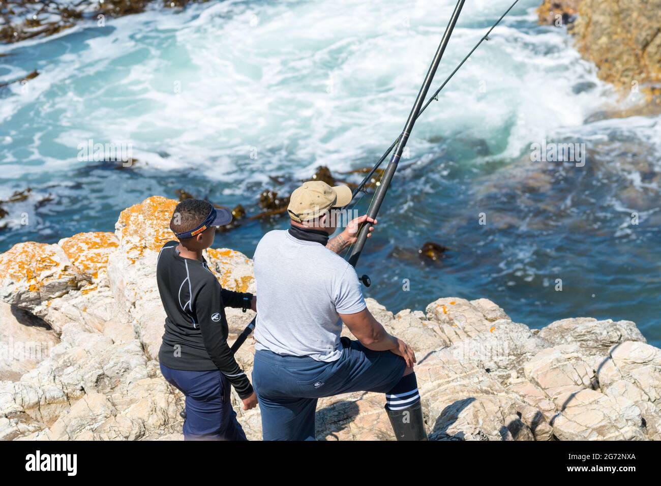 padre e figlio pescatori in piedi sulle rocce che si affacciano sull'oceano o l'acqua di mare che tengono pesca canne concetto di togetherness e stile di vita Foto Stock