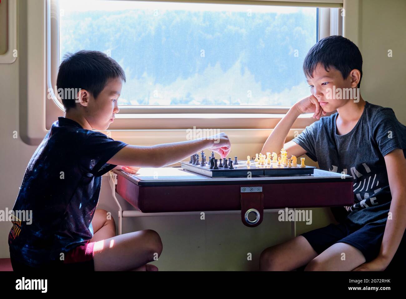 Ragazzi che giocano a scacchi vicino alla finestra in treno viaggio, concetto di giochi da tavolo Foto Stock