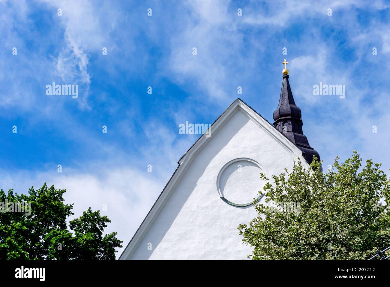 Una vista dettagliata di un edificio di chiesa imbiancato con campanile sotto un cielo blu con nuvole bianche e alberi verdi sotto Foto Stock