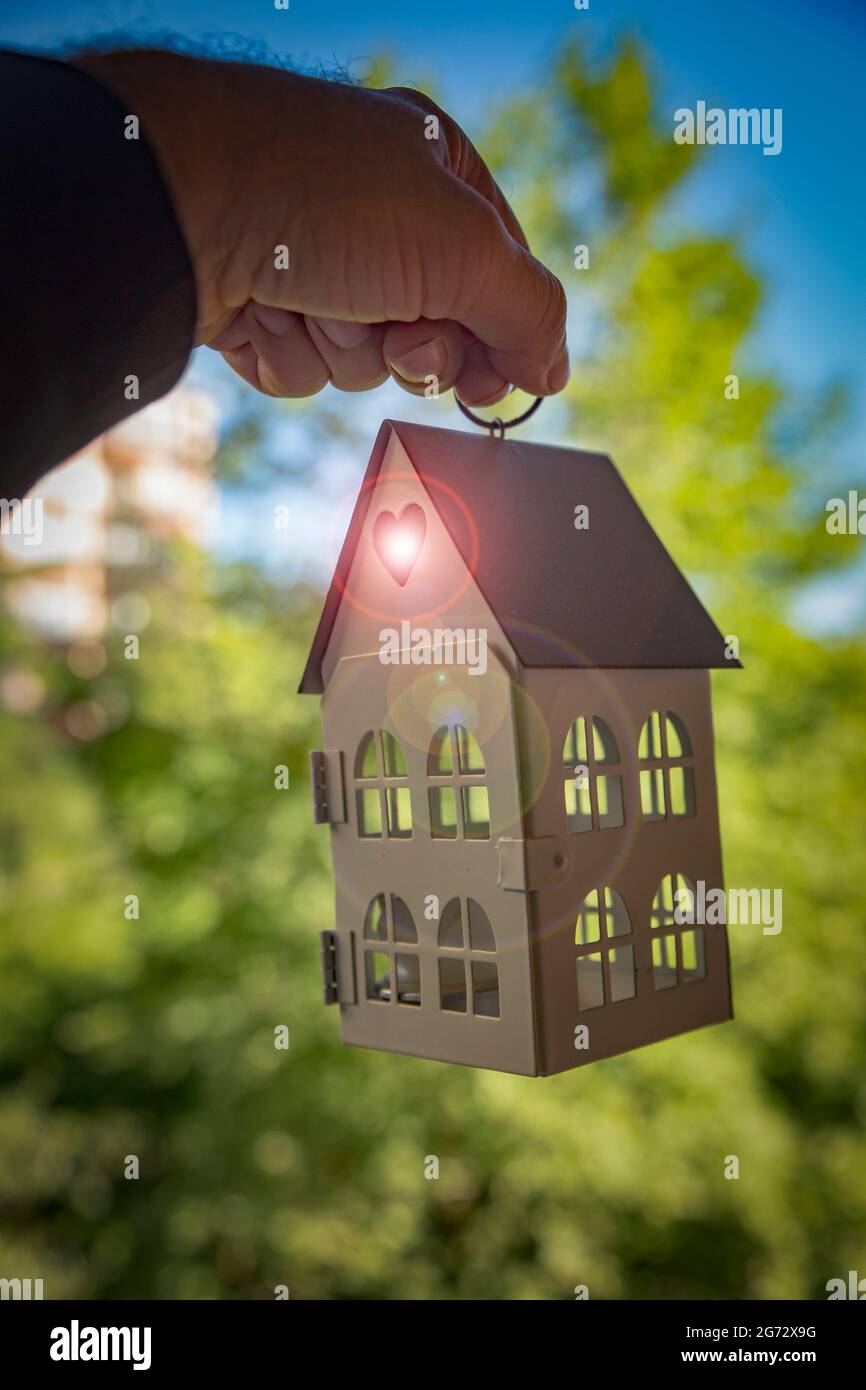 Housing Opportunity Concept con un modello di casa appeso alla mano di un uomo medio-orientale con un flare lente che esce da un foro a forma di cuore. Foto Stock