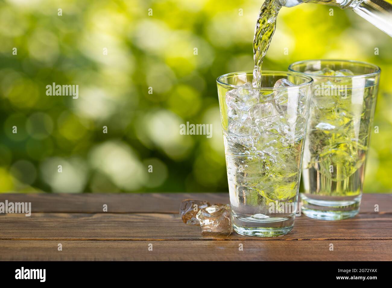 acqua dalla caraffa che si versa in vetro con cubetti di ghiaccio Foto Stock