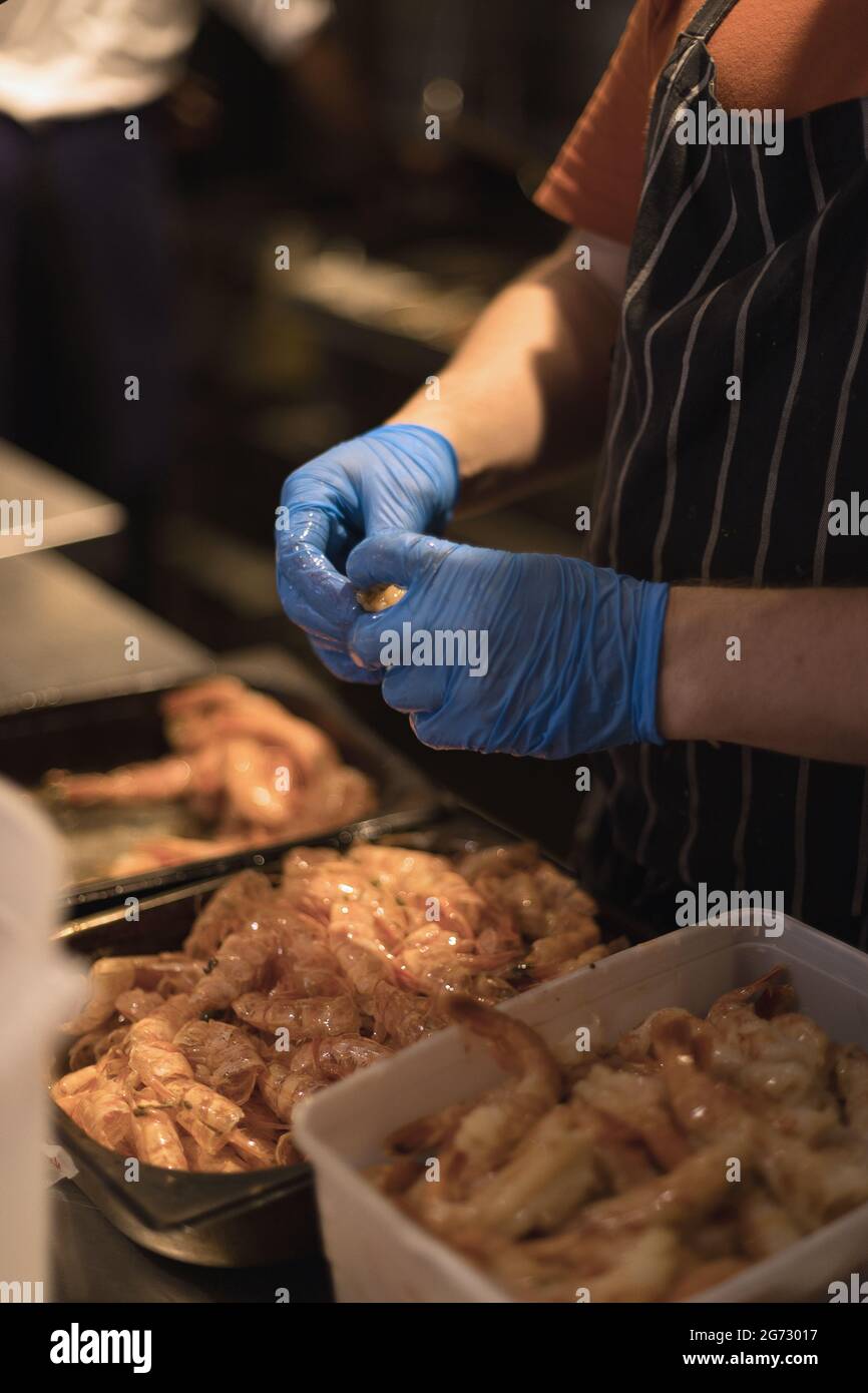 chef peeling gamberi con guanti blu Foto Stock