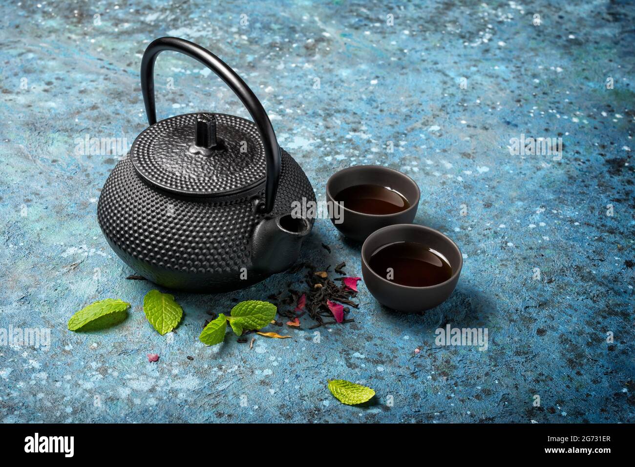 Teiera giapponese nera in ghisa e tè con foglie di menta verde su sfondo  blu in cemento con spazio per la copia Foto stock - Alamy