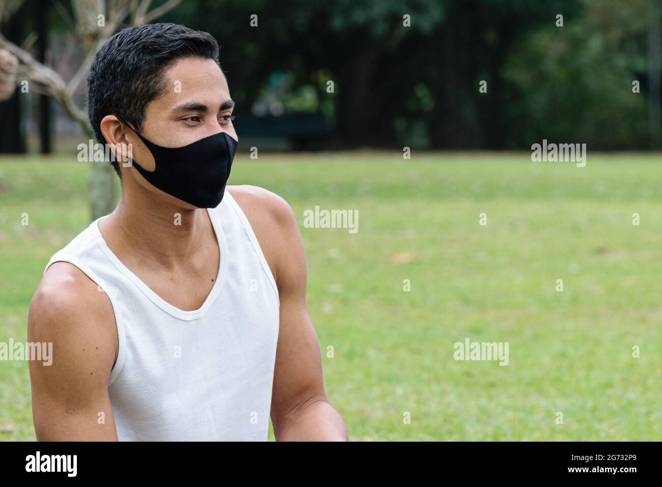Giovane brasiliano di 28 anni, indossando una maschera e seduto su un prato verde. Foto Stock