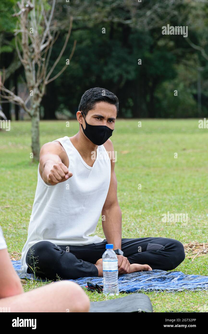 Giovane brasiliano di 28 anni, insegnante di yoga, con il pugno chiuso e seduto con le gambe incrociate. Foto Stock