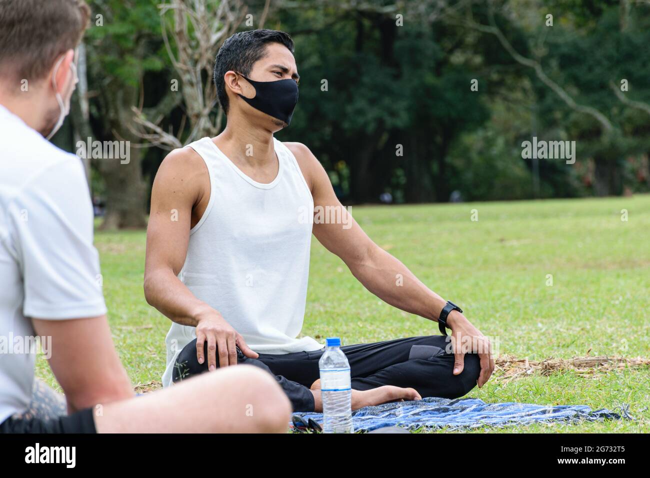 Giovane brasiliano di 28 anni, insegnante di yoga, seduto sul prato accanto ad una bottiglia d'acqua. Foto Stock