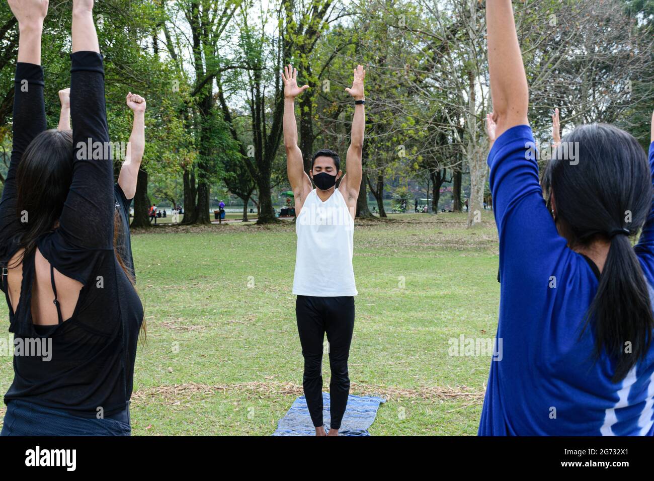Giovane brasiliano di 28 anni che dà lezioni di yoga, braccia su, in una giornata di sole nel parco pubblico. Foto Stock