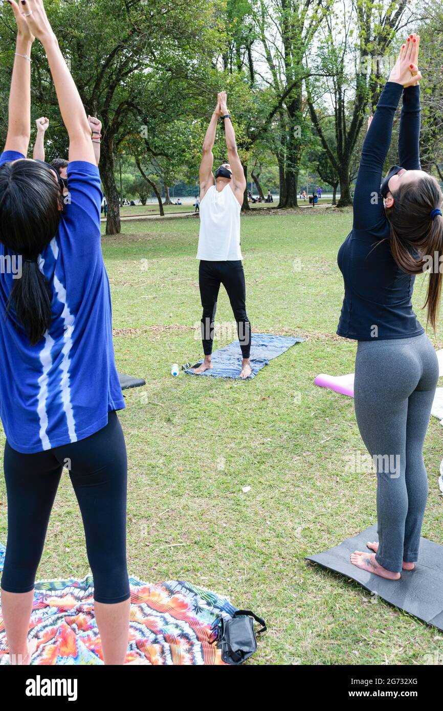 Sao Paulo, Sao Paulo, Brasile - Luglio, 04 2021: Giovane brasiliano di 28 anni, braccia in su, dando lezione di yoga nel parco pubblico Ibirapuera. Foto Stock
