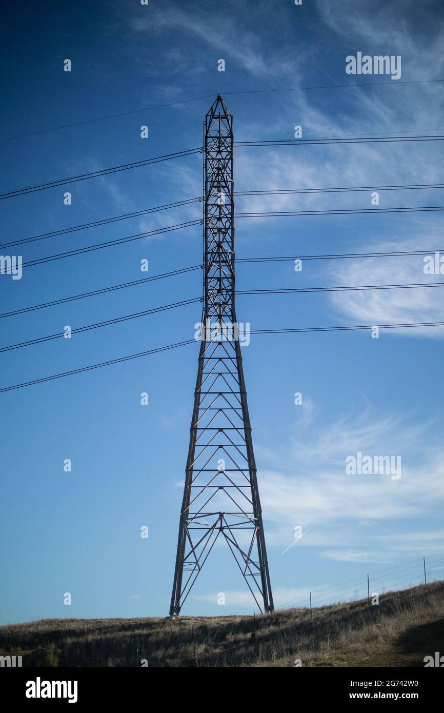 Torre di trasmissione elettrica con struttura a traliccio, collegata a linee elettriche che corrono in parallelo attraverso il cielo azzurro con alcune nuvole in autunno Foto Stock