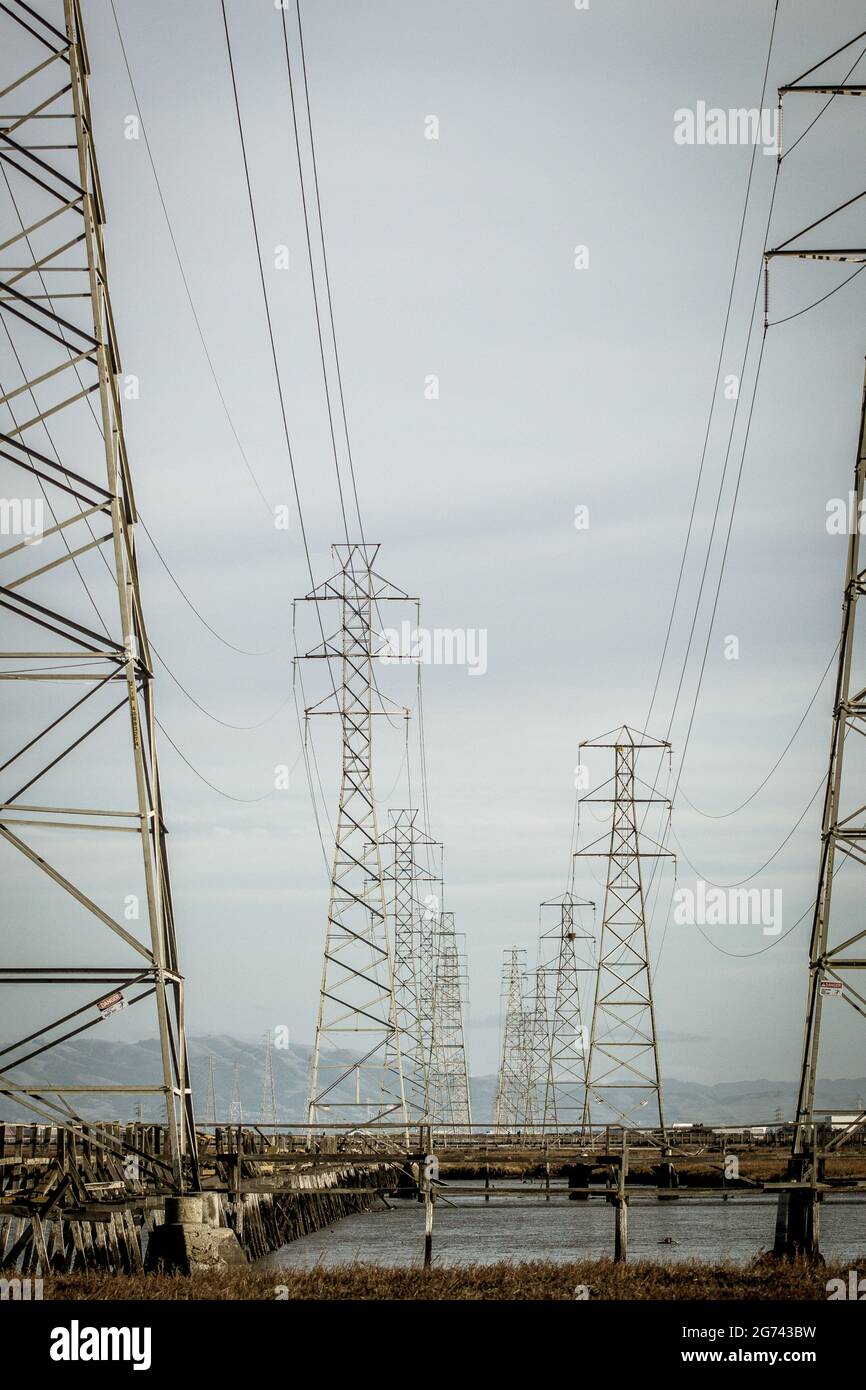 Serie di torri di trasmissione che attraversano la Baia di San Francisco collegate da cavi sospesi, fotografate in una giornata grigia con le montagne all'orizzonte Foto Stock