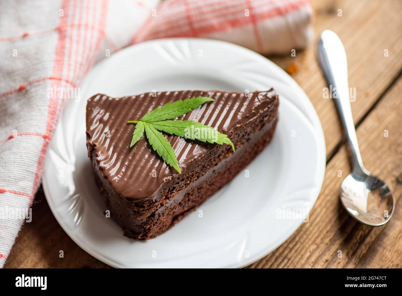 Chocolate cake with cannabis leaf - marijuana leaves plant on white plate on the wooden table, cannabis food nature herb concept Foto Stock