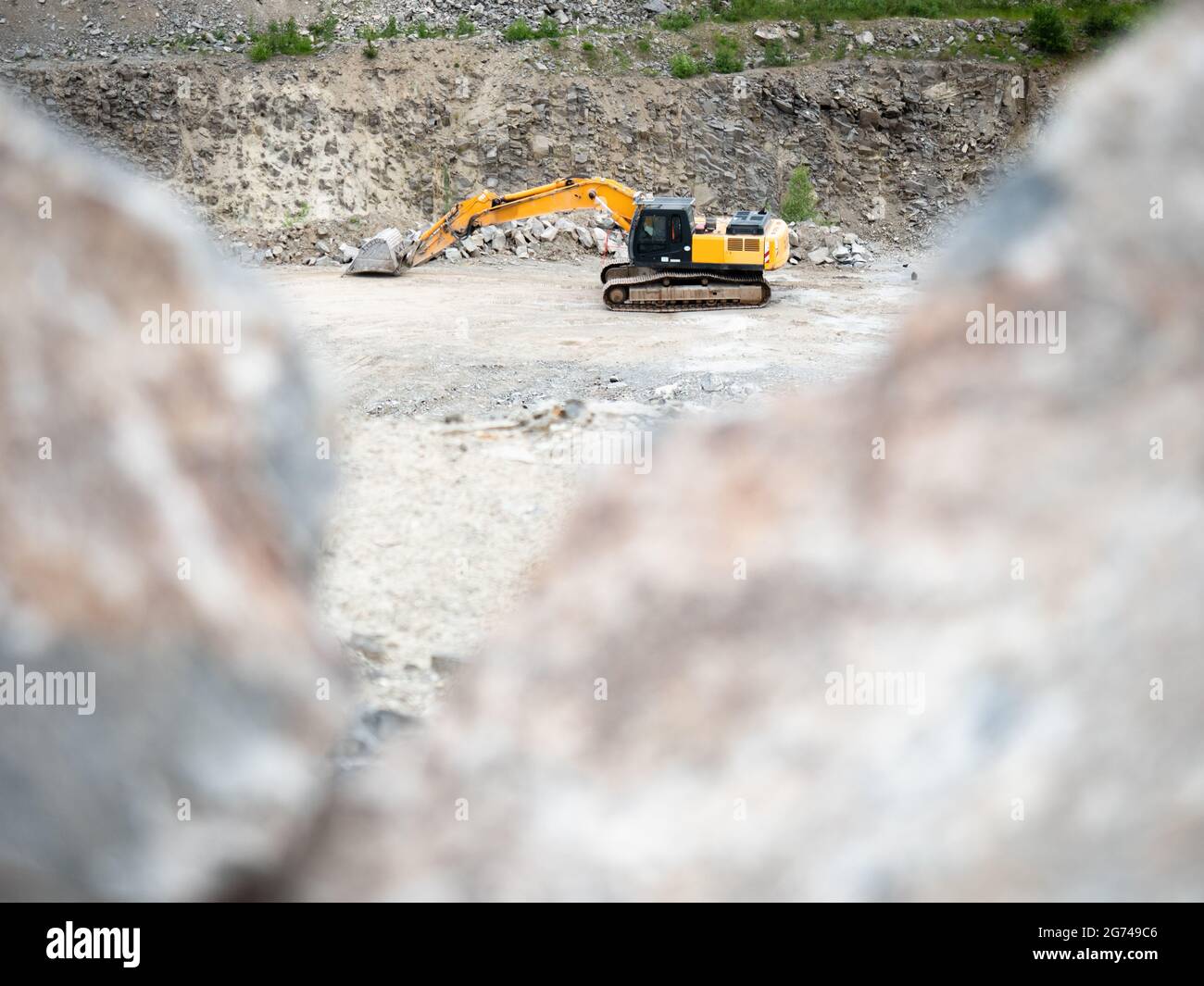 Escavatore pesante che lavora sul movimento terra in una miniera di granito  aperta. Macchina cingolata lavori di scavo in cava Foto stock - Alamy