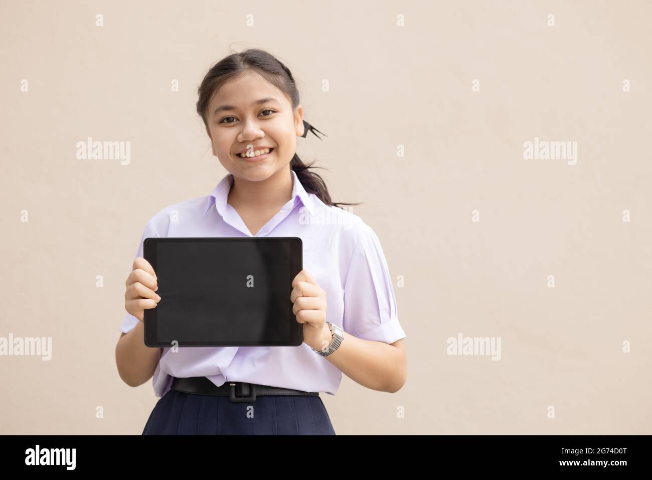 Asian ragazza teen studente mano tenere tablet vuoto spazio schermo per la pubblicità testo in uniforme scuola sorriso felice isolato. Foto Stock