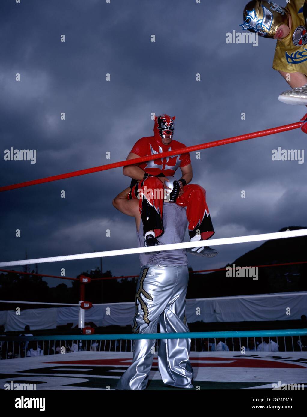 Uomini 'Luchadores' (lottatori) lottano a Ecatepec, alla periferia di Città del Messico. Il loro incontro è un riscaldamento per le donne wrestling. Cielo tempestoso annuncio Foto Stock