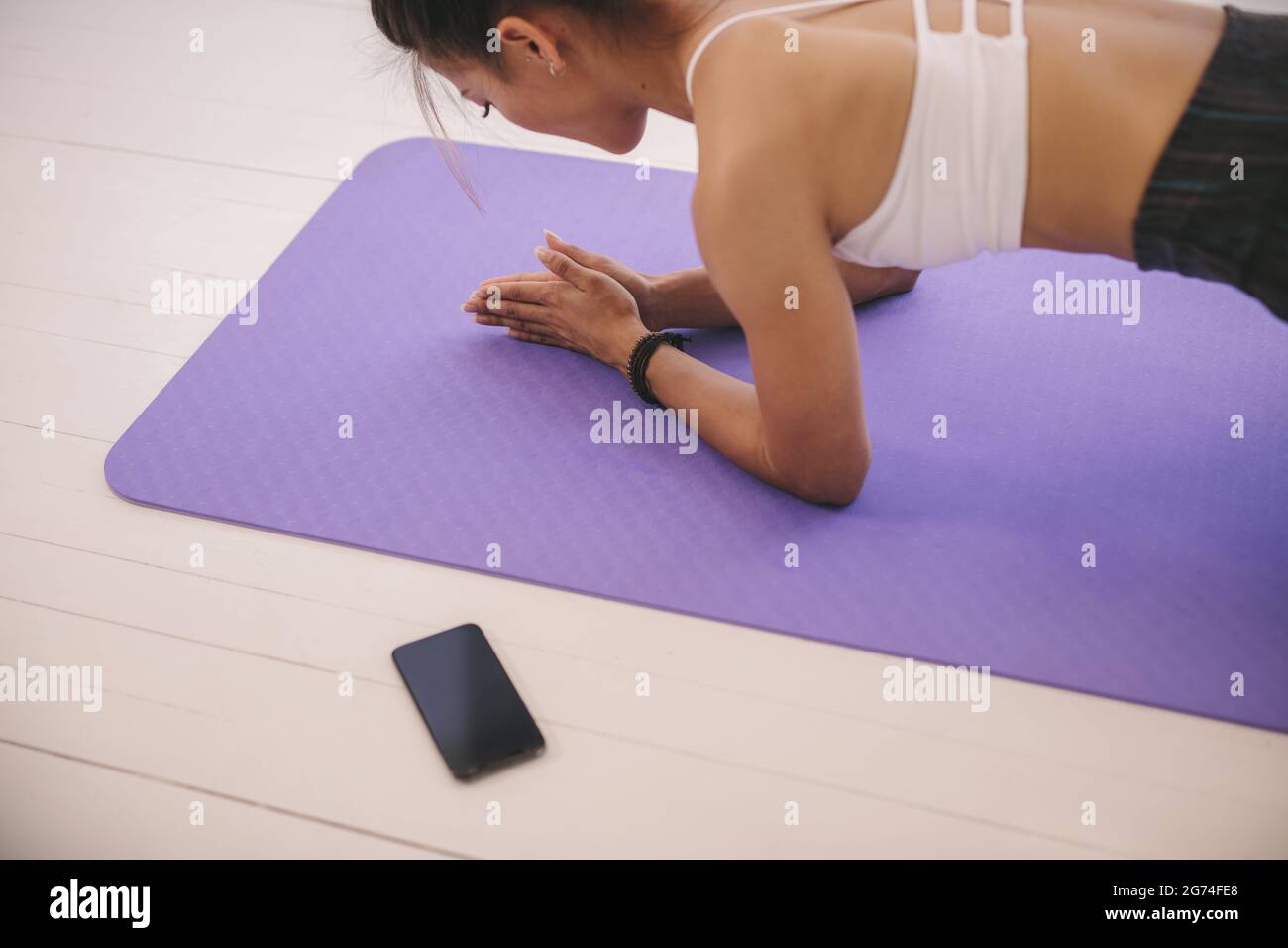 Giovane donna che fa esercizio core sul tappeto yoga in palestra con il suo telefono cellulare sul lato. Posizione della tavola di tenuta femminile in studio di fitness. Foto Stock