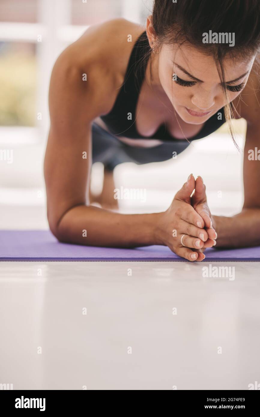 Giovane donna che fa l'esercitazione principale sul tappeto di idoneità nella palestra. Posizione della tavola di tenuta femminile in studio di fitness. Foto Stock