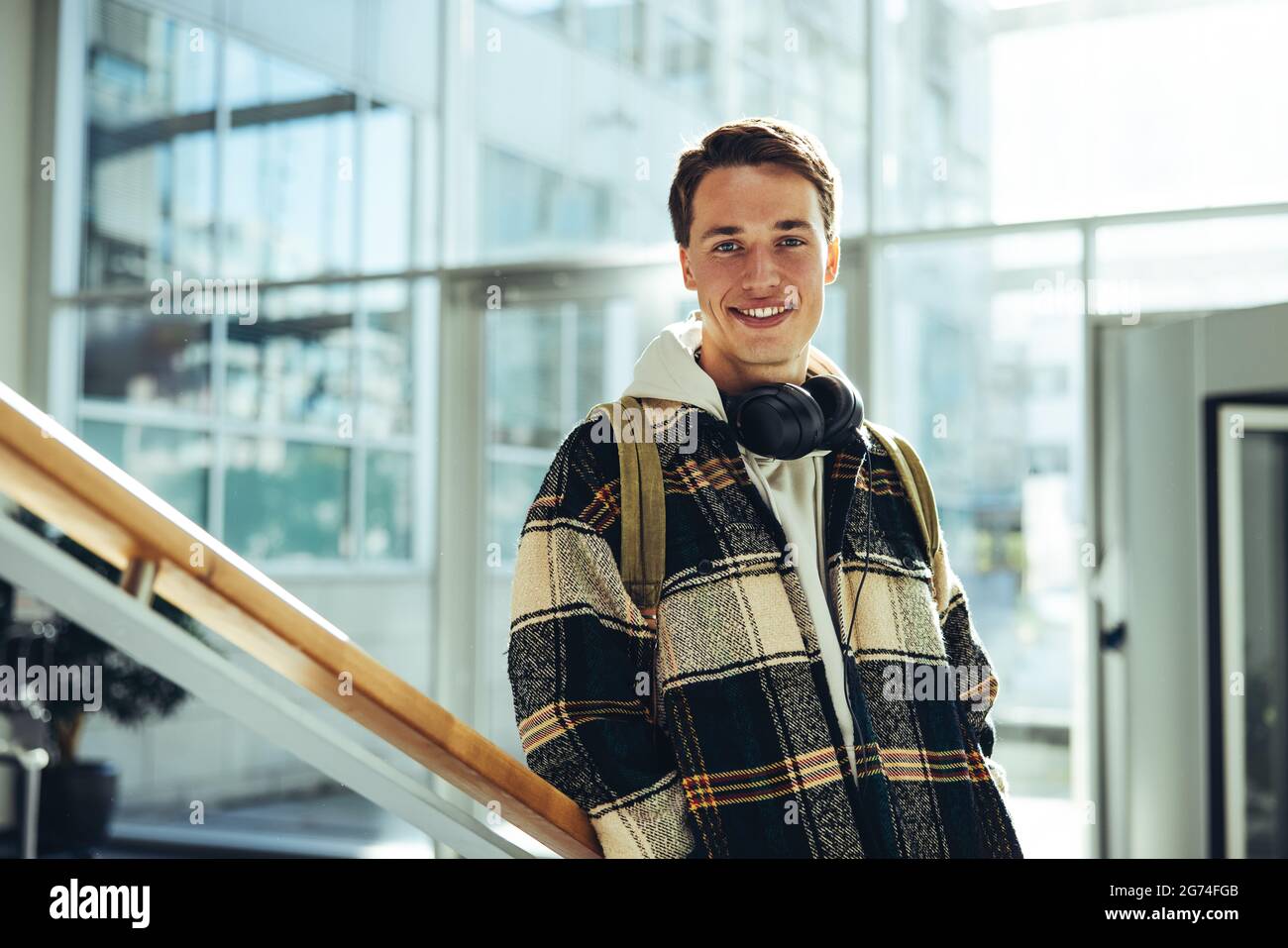 Studente alle scale del college sorridente. Giovane uomo sorridente alla macchina fotografica mentre si appoggia alle scale ringhiera in università. Foto Stock