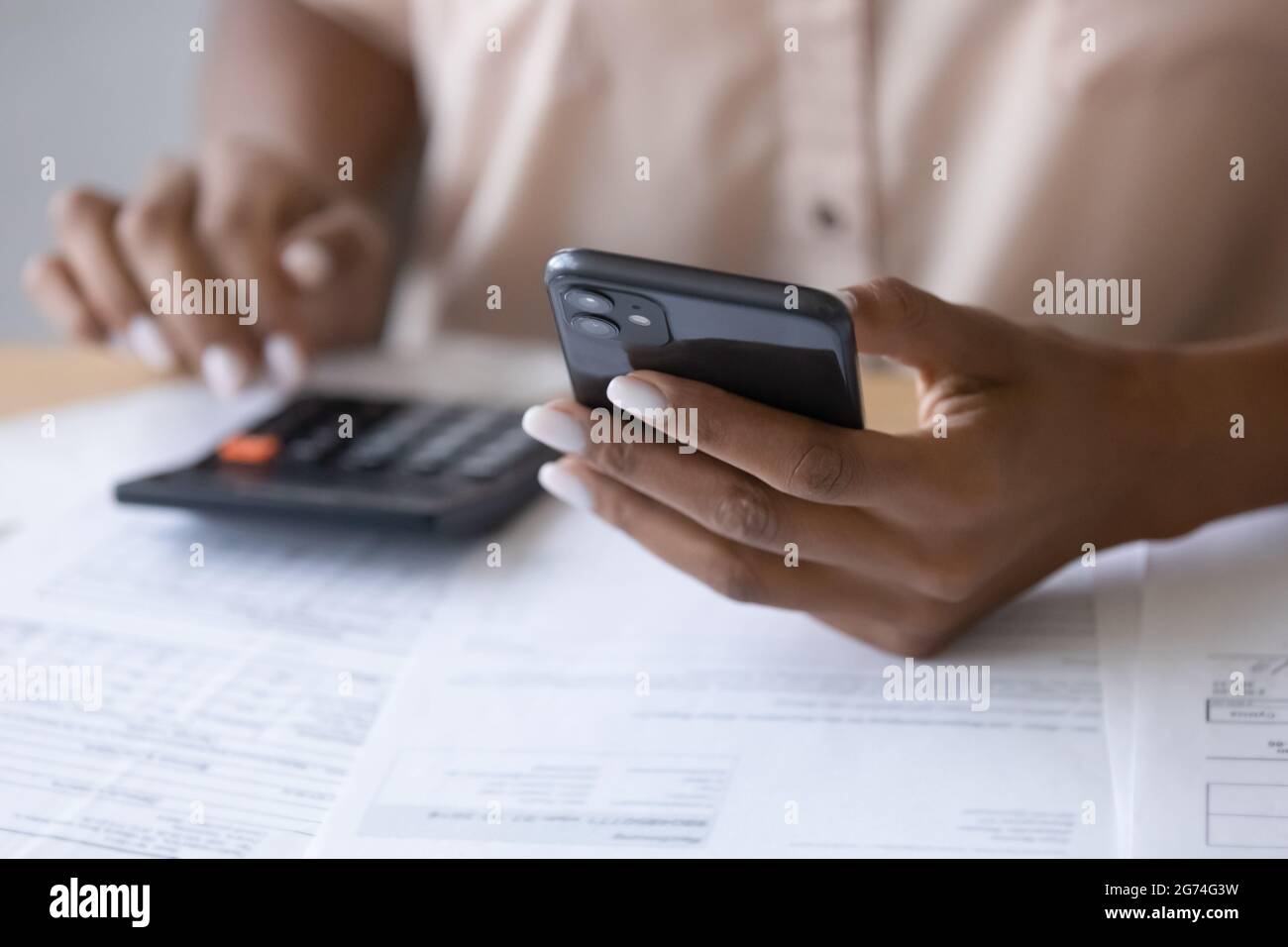 Primo piano donna afroamericana utilizzando smartphone, calcolando le fatture Foto Stock