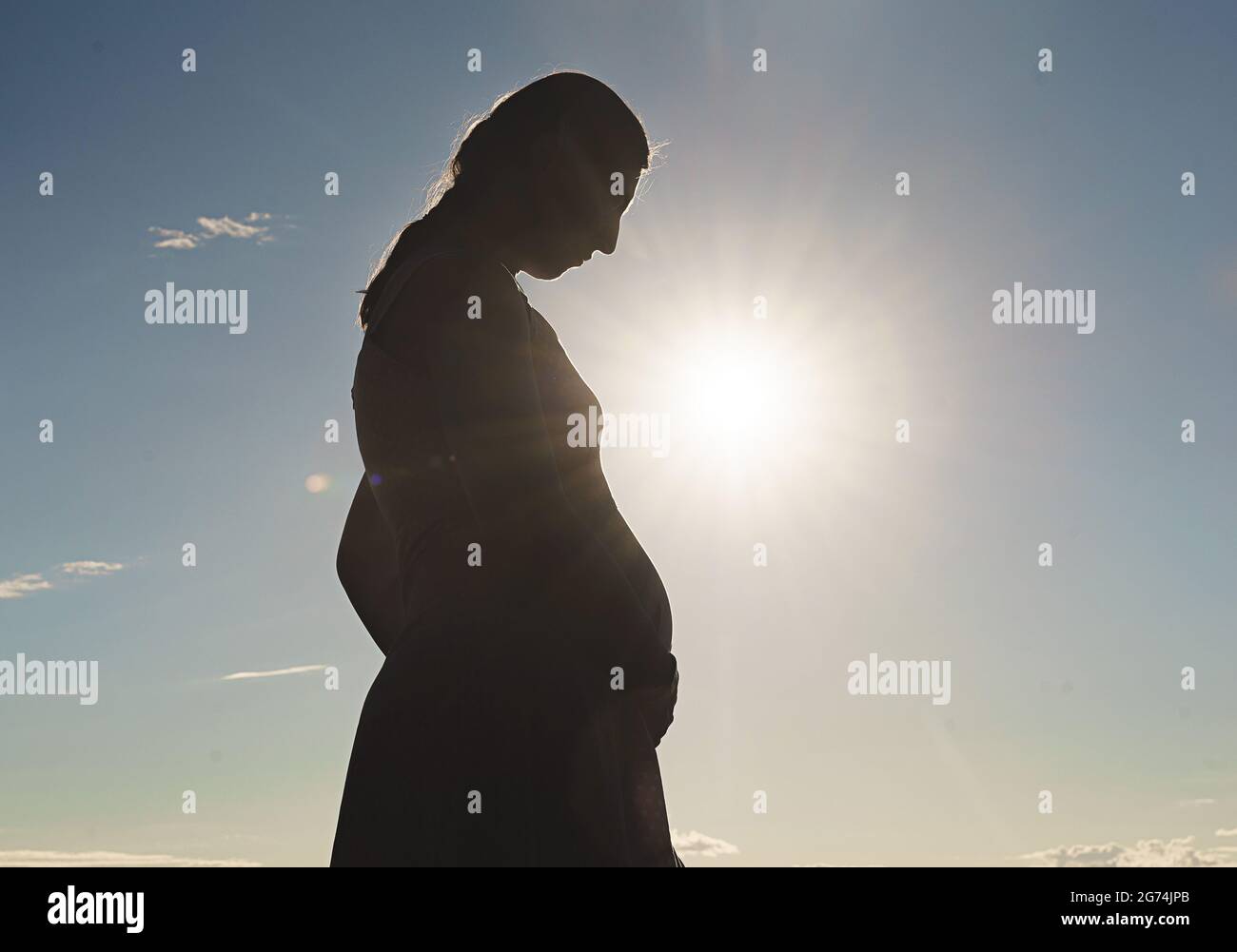 Silhouette di una donna incinta su uno sfondo di cielo blu e sole luminoso. Foto Stock