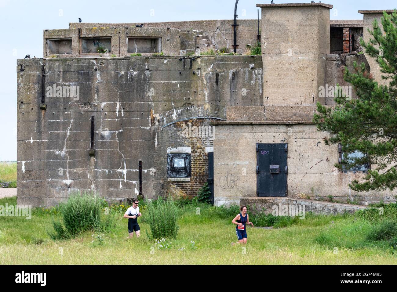 I corridori che gareggiano nel Southend Triathlon 2021 a Shoeburyness, Essex, Regno Unito, correndo attraverso la riserva naturale di Gunners Park passato l'emplement delle armi in tempo di guerra Foto Stock