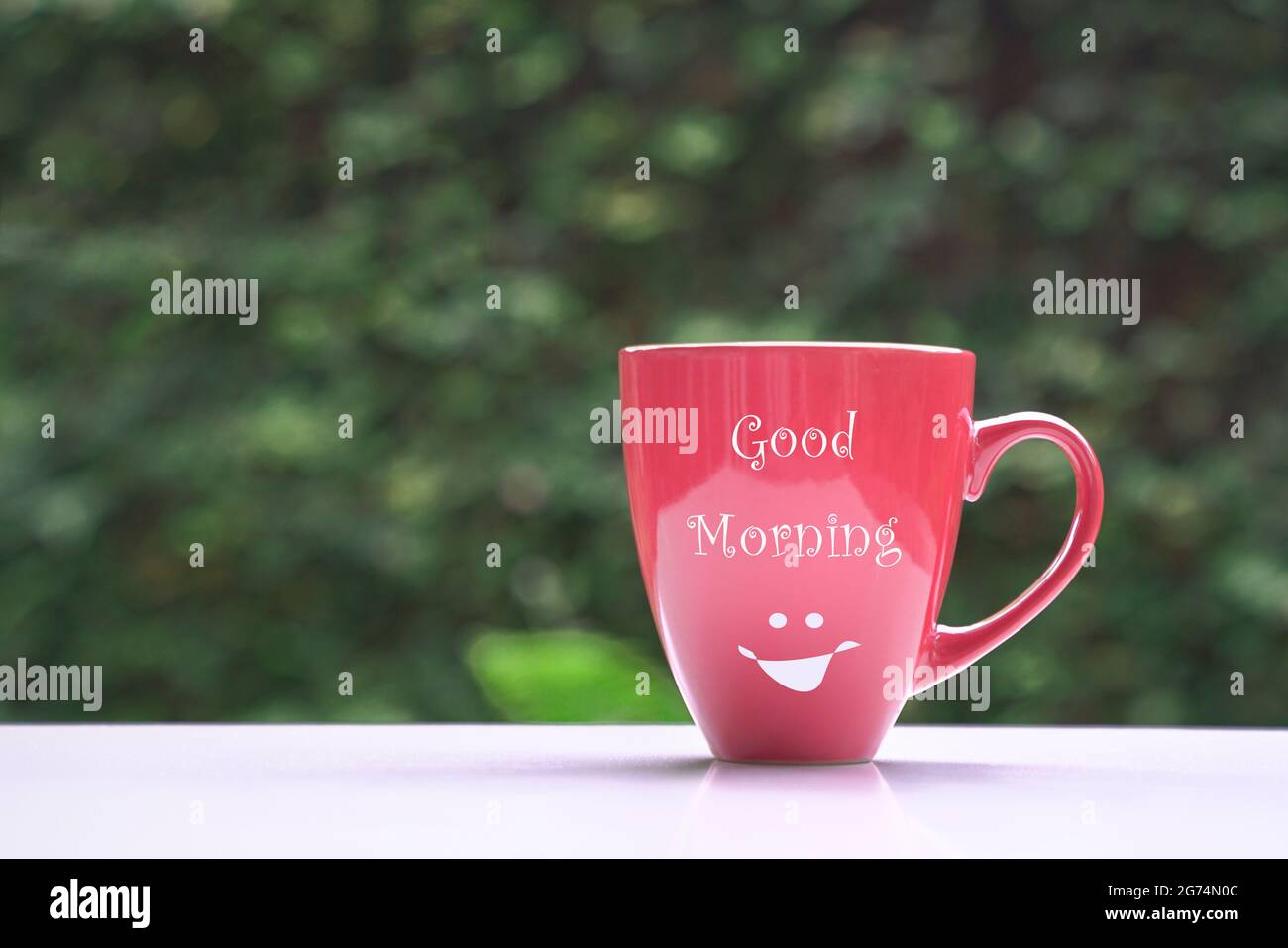 Buon messaggio del mattino sulla tazza di caffè rossa, su sfondo verde natura. Spazio di copia. Foto Stock
