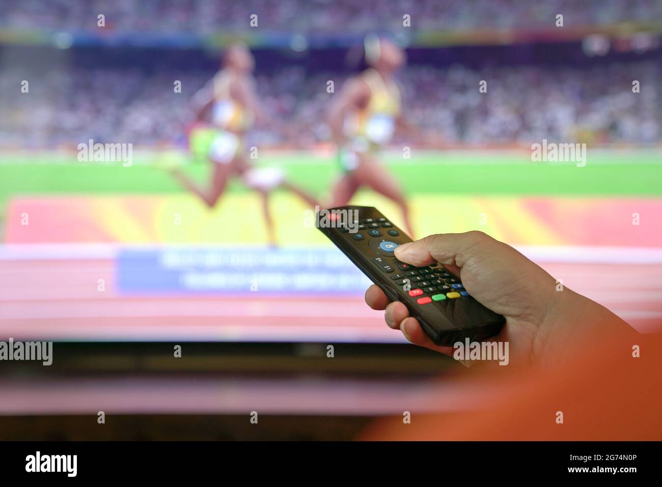 Uomo guarda la pista sportiva e il campo in tv. Vista ravvicinata sul telecomando. Foto Stock