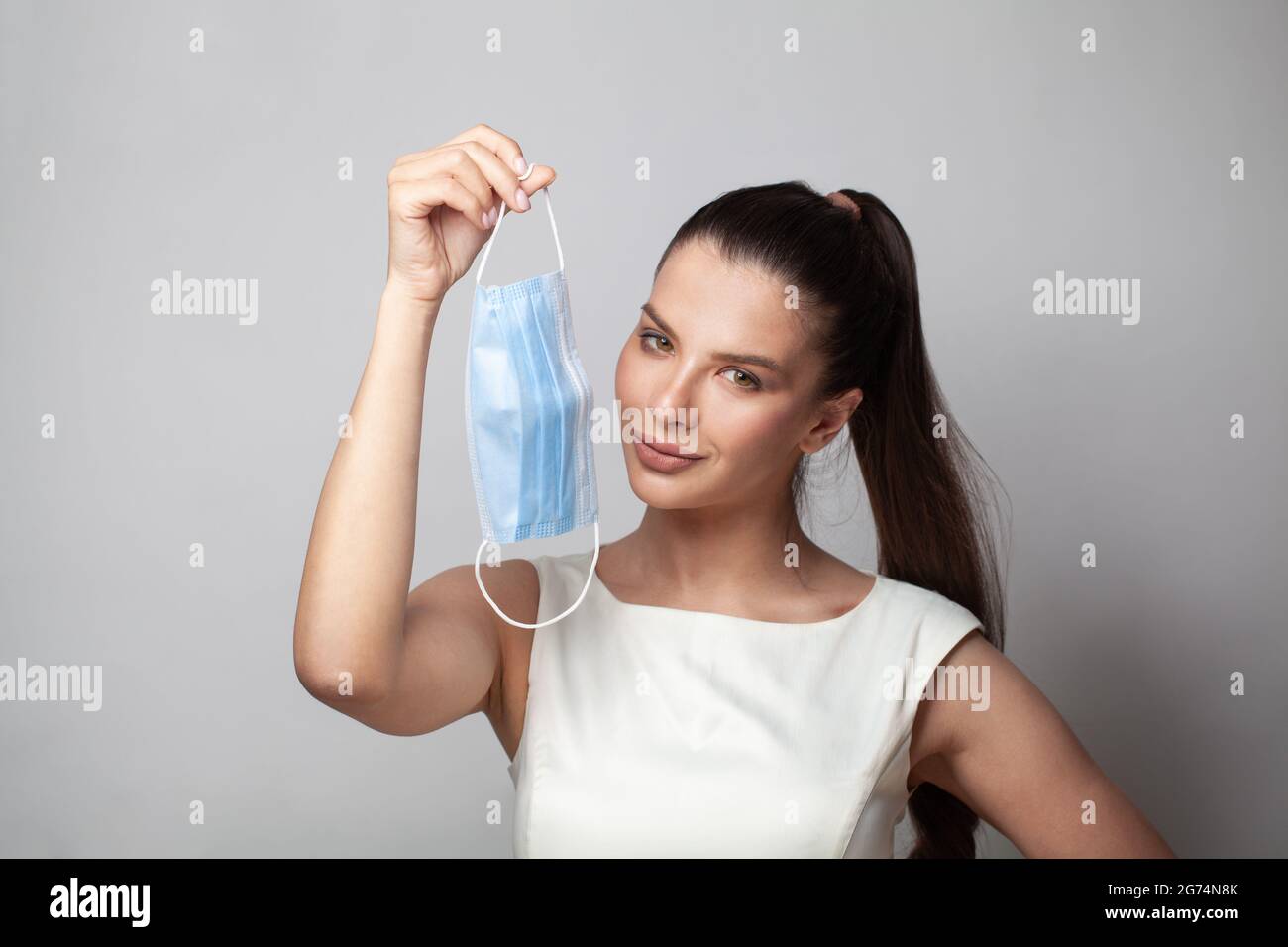 Dopo la pandemia, epidemia, influenza stagionale. Giovane donna positiva con una maschera medica in mano sorridente. Felice modello femminile togliendo la sua maschera Foto Stock
