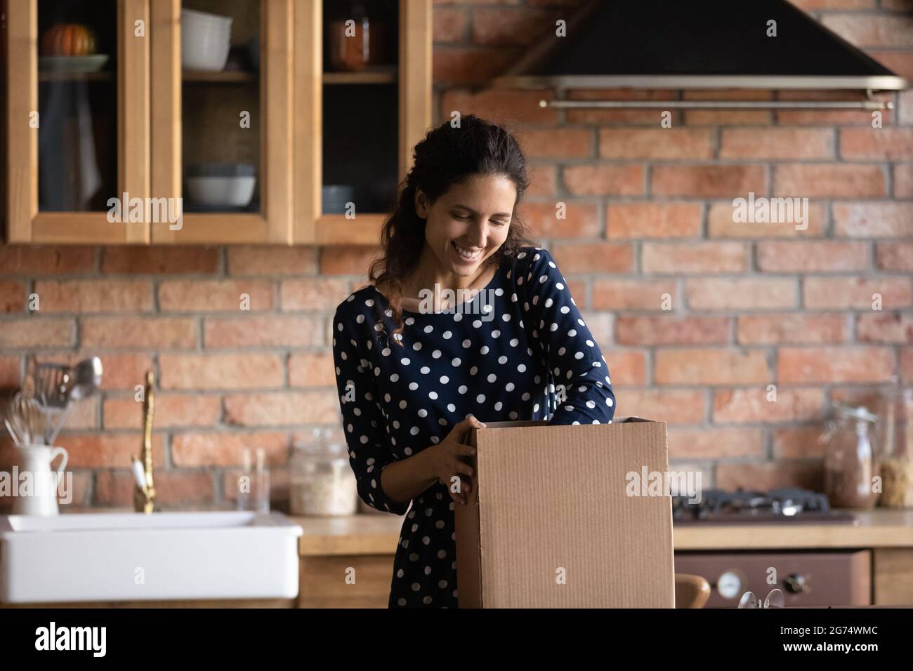 Donna felice che disimballo scatola di cartone in cucina Foto Stock