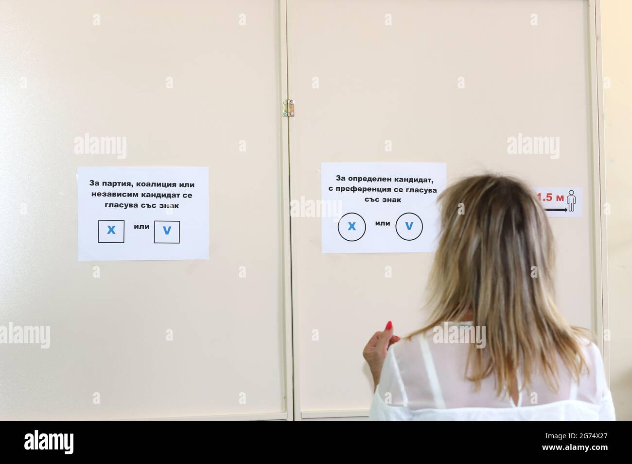 Le persone con maschere stanno usando una macchina di voto nelle elezioni parlamentari bulgare a Sofia, Bulgaria, il 11 luglio 2021 Foto Stock