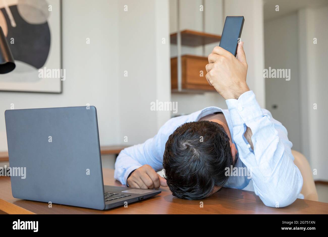 Frustrato uomo di mezza età che lavora da casa, di fronte al laptop, tenendo un telefono lontano dalle orecchie Foto Stock