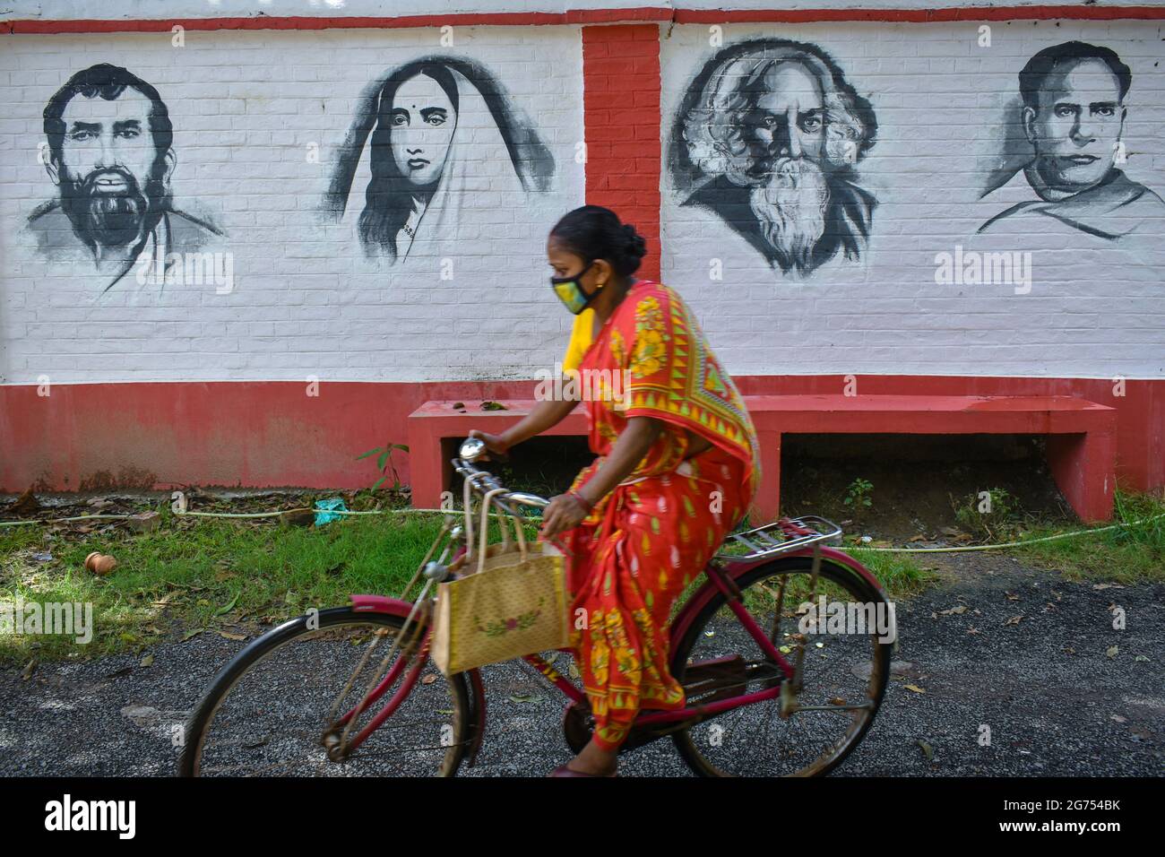 Kolkata, India. 11 Luglio 2021. Una donna che cavalcava in bicicletta accanto ad un murale di personaggi famosi (da sinistra - Sri Ramakrishna, Sarada Devi, Rabindranath Tagore e Ishwar Chandra Vidyasagar) dell'India una gonna a Kolkata. (Foto di Sudipta Das/Pacific Press) Credit: Pacific Press Media Production Corp./Alamy Live News Foto Stock