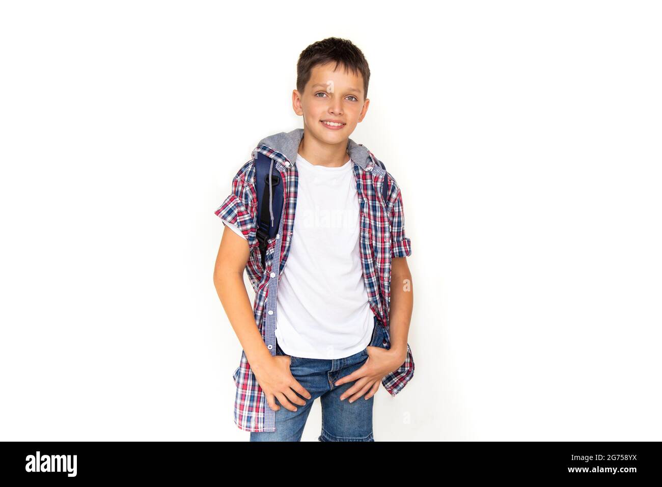 Ragazzo adolescente 11 anni scolaro guardando la macchina fotografica su sfondo bianco con zaino e sorridente. Vestita con camicia in plaid e t-shirt bianca, copy sp Foto Stock