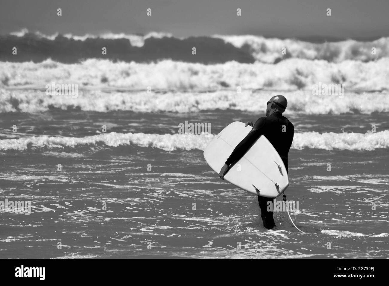 I surfisti di tutte le età portano tavole da surf sul bordo dell'acqua della spiaggia di Llangennith sulla penisola di Gower. Immagine monocromatica che raffigura attività all'aperto Foto Stock