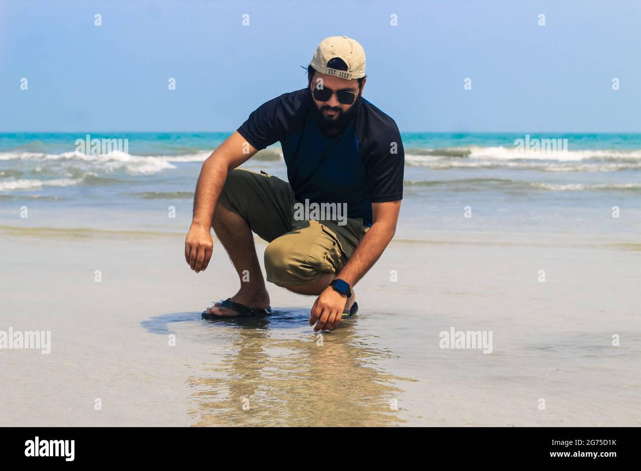 Il giovane al mare raccoglie conchiglie sulla spiaggia, tramonto, vacanze estive in mare o in oceano. Un ragazzo sulla spiaggia che raccoglie conchiglie. Foto Stock