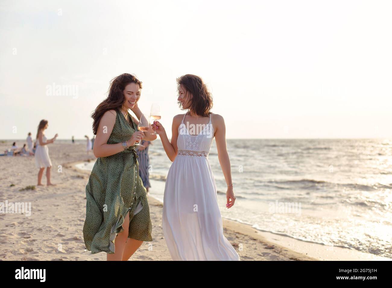 Felice adulta femmina amici in estate vestito sorridendo mentre godendo il vino sulla spiaggia di sabbia vicino al mare Foto Stock