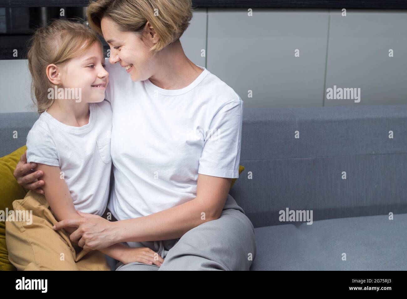 Mamma e figlia che si abbracciano sul divano guardano gli uni negli altri Foto Stock