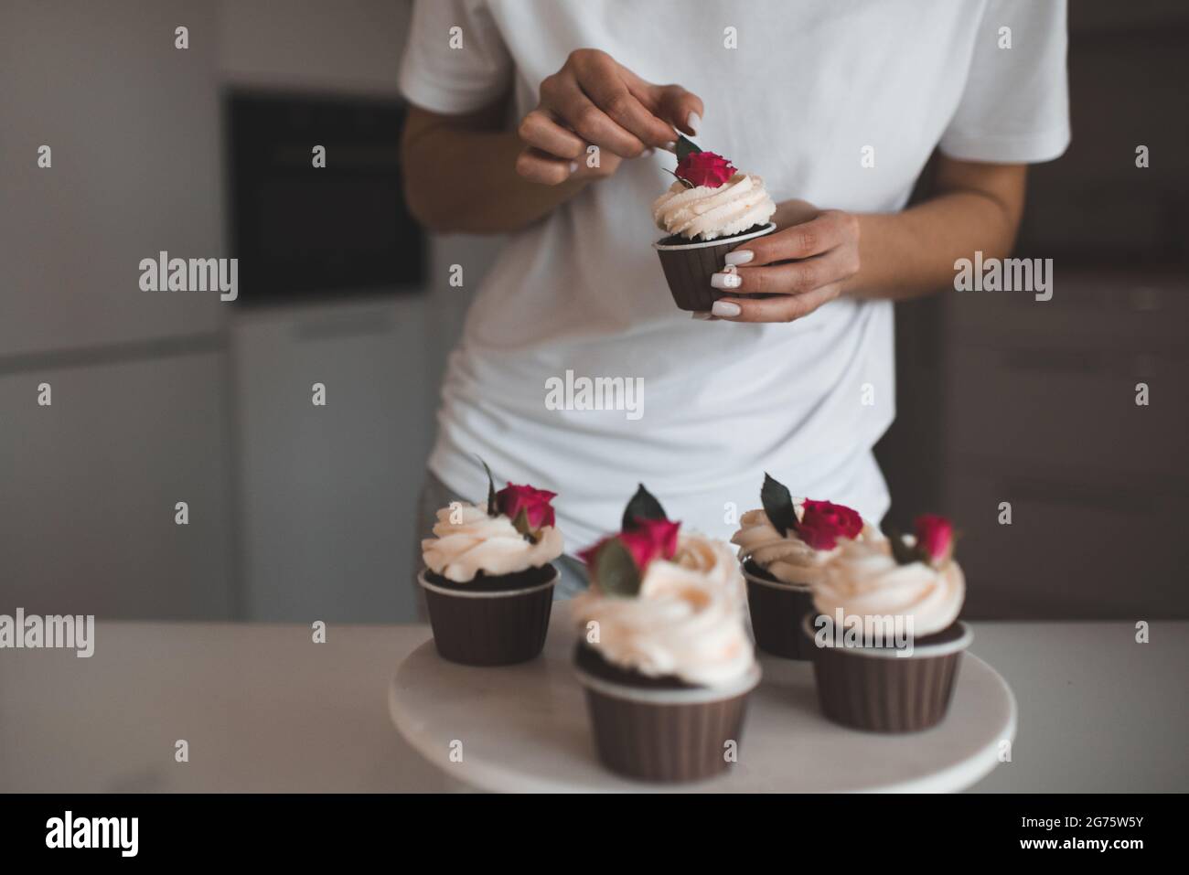 Donna decorare cremoso torta tazza di cioccolato con rose di fiori freschi rimanere su vassoio bianco in cucina primo piano. Foto Stock