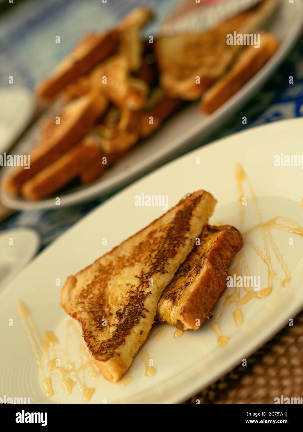 Due toast alla francese serviti con miele su un piatto bianco per colazione o brunch, sullo sfondo una pila di toast alla francese. Foto Stock