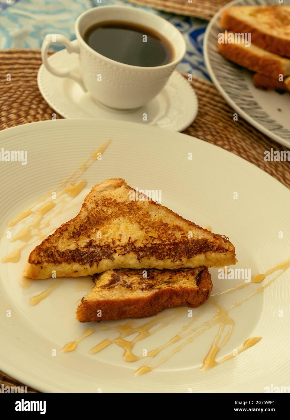 Due toast alla francese serviti con miele su un piatto bianco per colazione o brunch, sullo sfondo una tazza di caffè nero e una pila di toast alla francese. Foto Stock