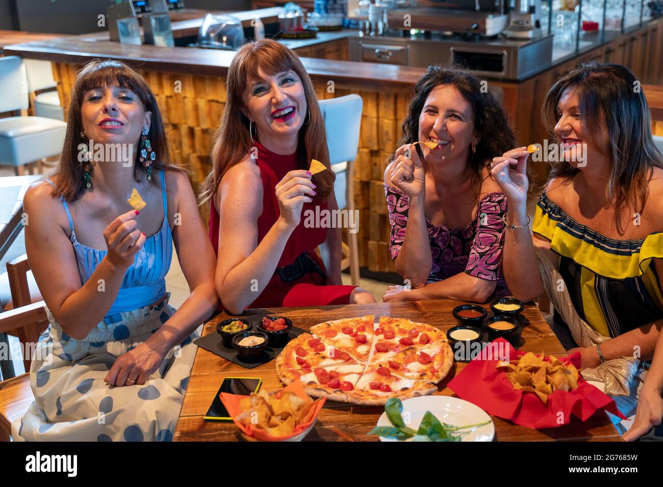 gruppo di donne mature che si siedono in un pub mentre mangiano la pizza e bevono la birra Foto Stock