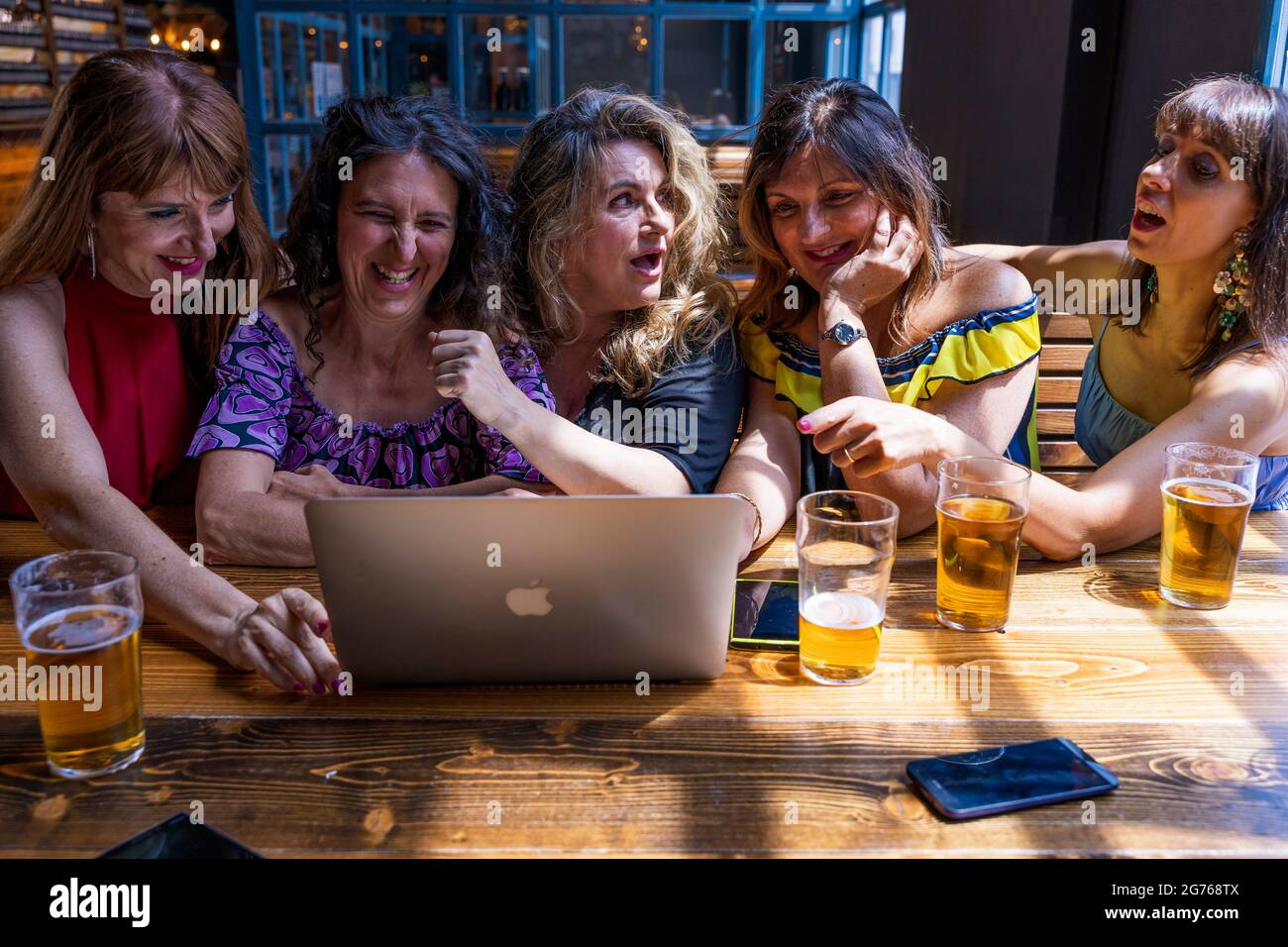 gruppo di amici di sesso femminile che si divertono a bere birra e guardare il computer in un pub Foto Stock