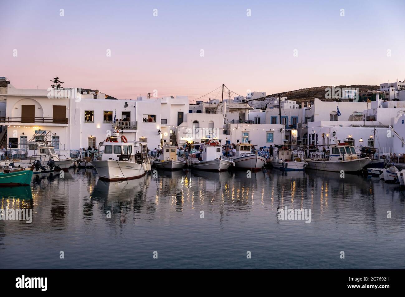 Grecia, Paros isola Naousa vecchio porto. 19 maggio 2021. Tipiche barche da pesca ormeggiate presso il molo del porto, la gente al tradizionale caffè all'aperto e ristorante Foto Stock