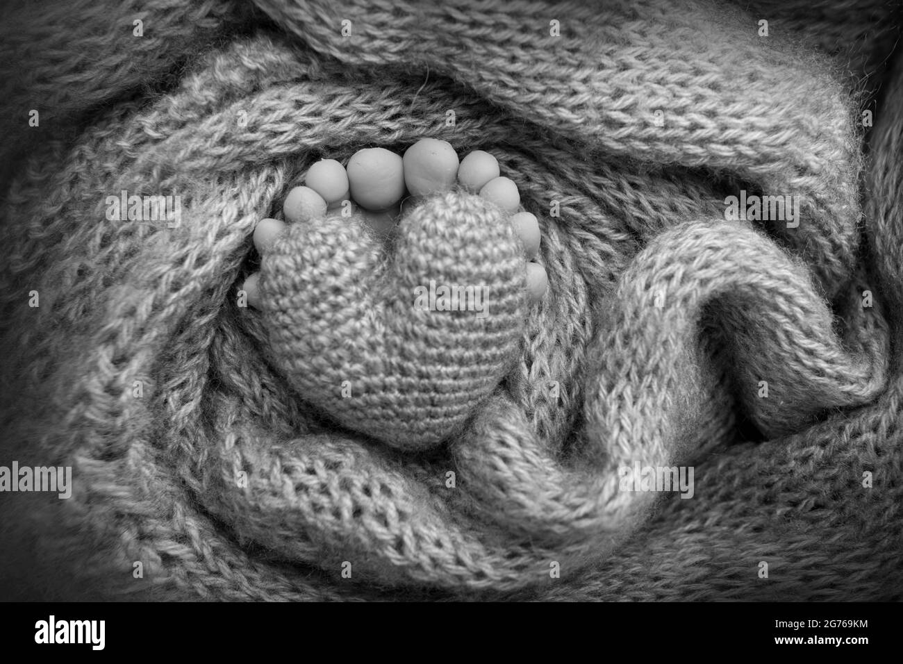 Piedi di un neonato con un cuore di legno, avvolto in una morbida coperta. Bianco-nero. Foto Stock