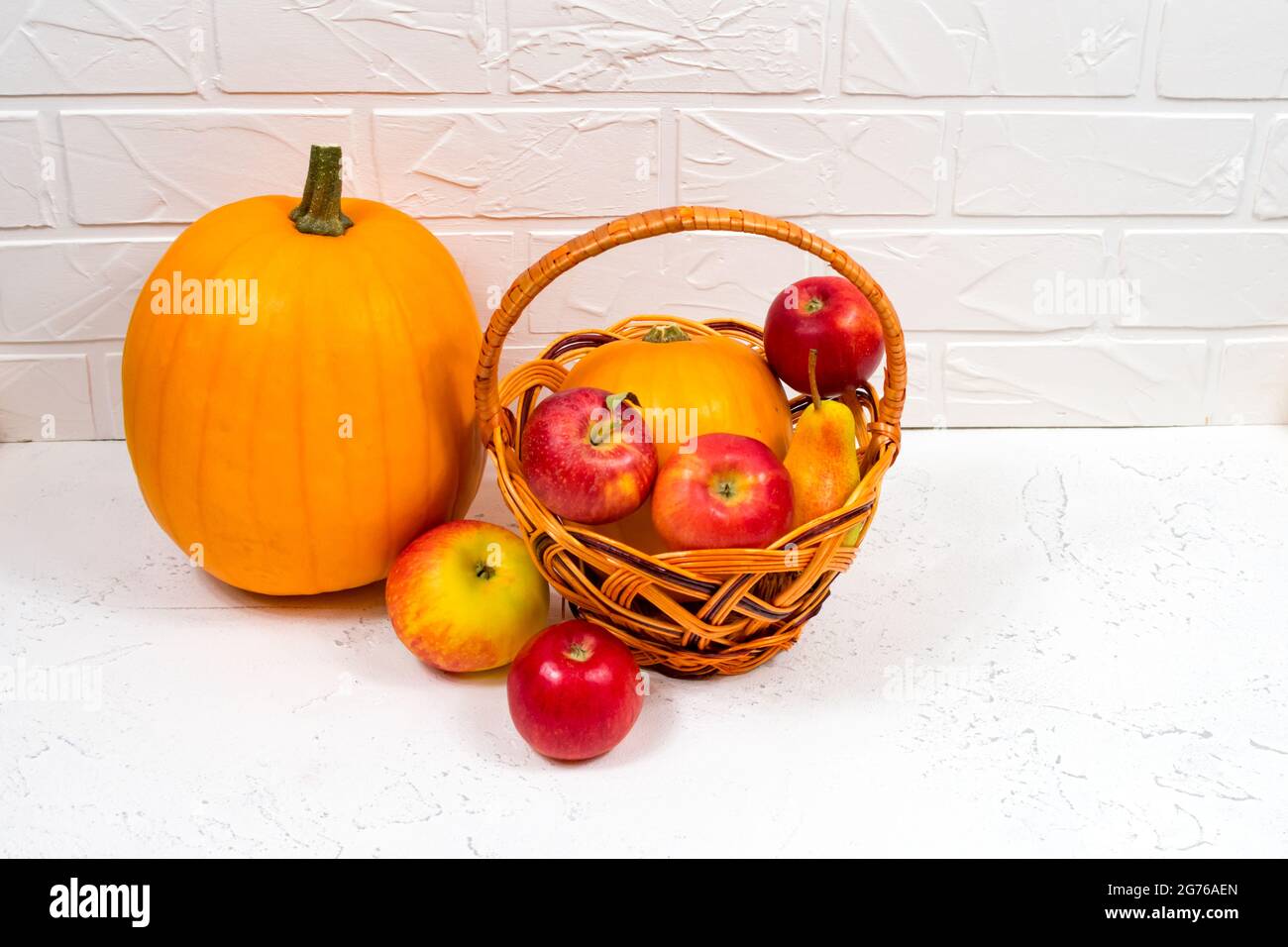 Zucche arancioni con mele e pere in un cesto di vimini su sfondo bianco. Autunno ancora vita. Foto Stock