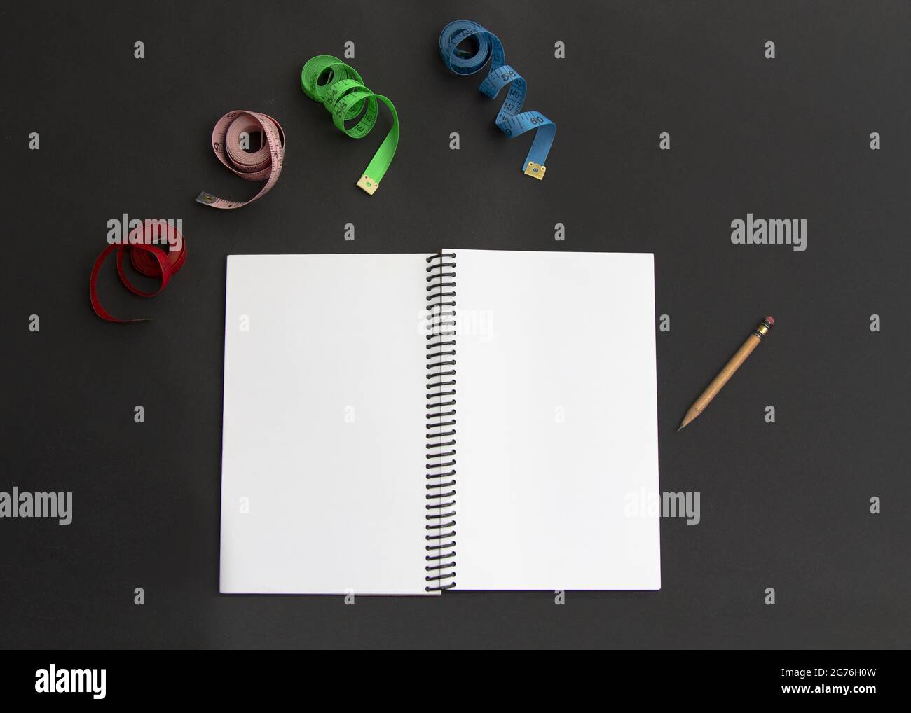 Immagine in primo piano di un notebook con una matita e centimetri multicolore su uno sfondo nero Foto Stock